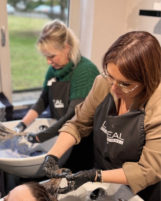 Julia K. und Julia E. bei der Arbeit im Friseursalon Juliko in Ansbach. Sie tragen Kundinnen Farbe am Waschbecken auf.